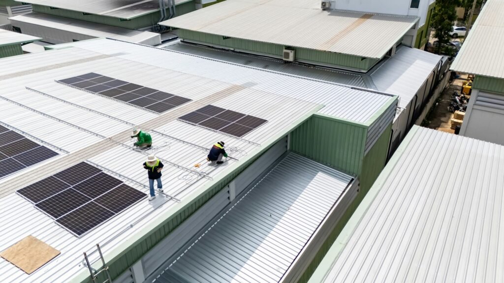 Men technicians mounting photovoltaic solar moduls on rooftop of warehouse.